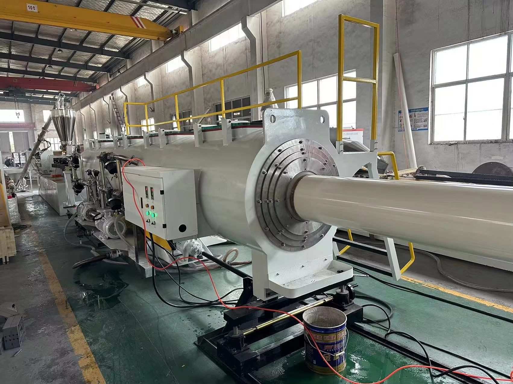 Continuous extruded plastic pipe passing through a long stainless steel vacuum calibration and cooling water bath.